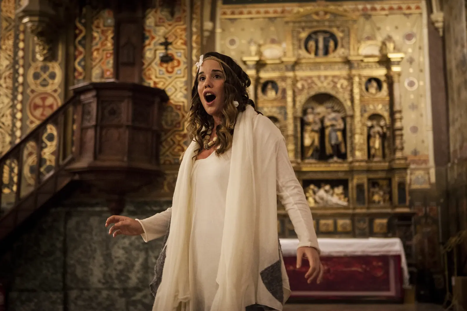 Isabel in white, singing before the gilded altarpiece