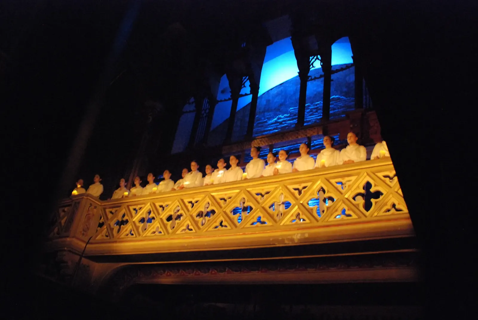 The choir in white along the carved gallery, lit gold against blue